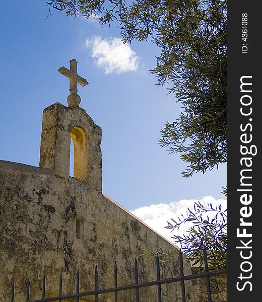 A limestone church against a blue sky framed by an olive tree. A limestone church against a blue sky framed by an olive tree