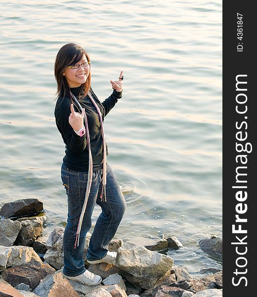 Teenager girl making hand signals with fingers at a rocky water's edge. Teenager girl making hand signals with fingers at a rocky water's edge