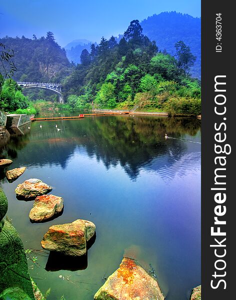 A beautifuk lake with stepping stones from the Wudang Shan mountain in the Hubei district in China. Lush vegetation and mountains in the background. A beautifuk lake with stepping stones from the Wudang Shan mountain in the Hubei district in China. Lush vegetation and mountains in the background.
