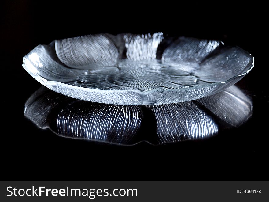 A glass plate of lotus shape,with engraved patterns, reflection on the table.