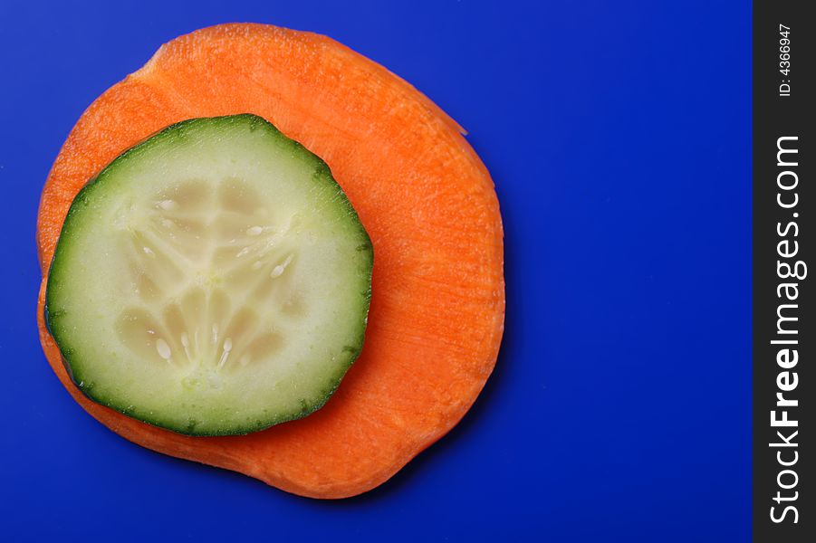 Carrots and cucumber on a dark blue background. Bright paints of a fresh product. Carrots and cucumber on a dark blue background. Bright paints of a fresh product