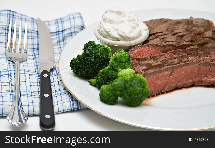 A plate of rare beef with sides of whipped horseradish sauce and broccoli. A plate of rare beef with sides of whipped horseradish sauce and broccoli