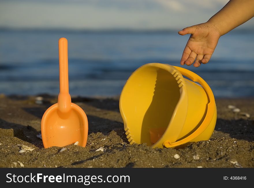 Beach toys and child's hand by the sea shore. Beach toys and child's hand by the sea shore