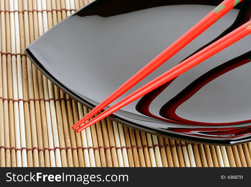 Red chopsticks and black dish on a bamboo mat. Close-up. Variant two. Red chopsticks and black dish on a bamboo mat. Close-up. Variant two.