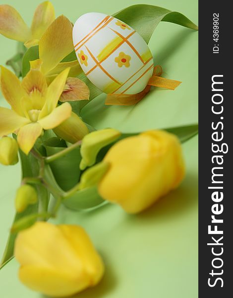 Easter egg with yellow tulip and yellow orchid on green background.