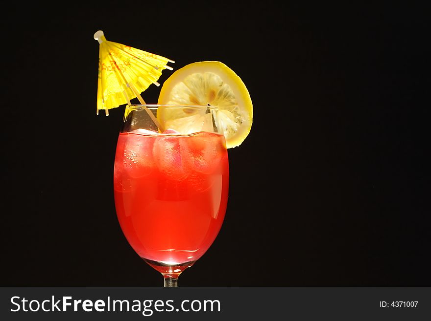 Colorful alcoholic cocktail in a tall glass with lemon and umbrella against black background