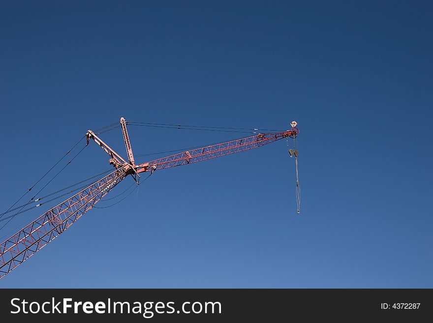 A red crane against a blue sky with a pulley attached. A red crane against a blue sky with a pulley attached