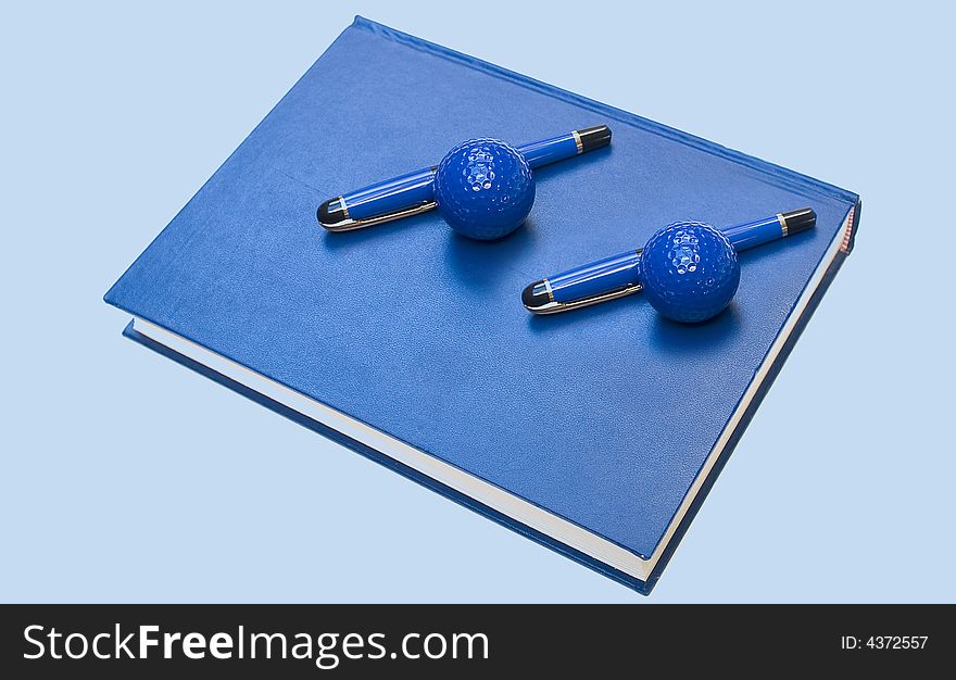 Golf balls and pens on book and blue background. Golf balls and pens on book and blue background