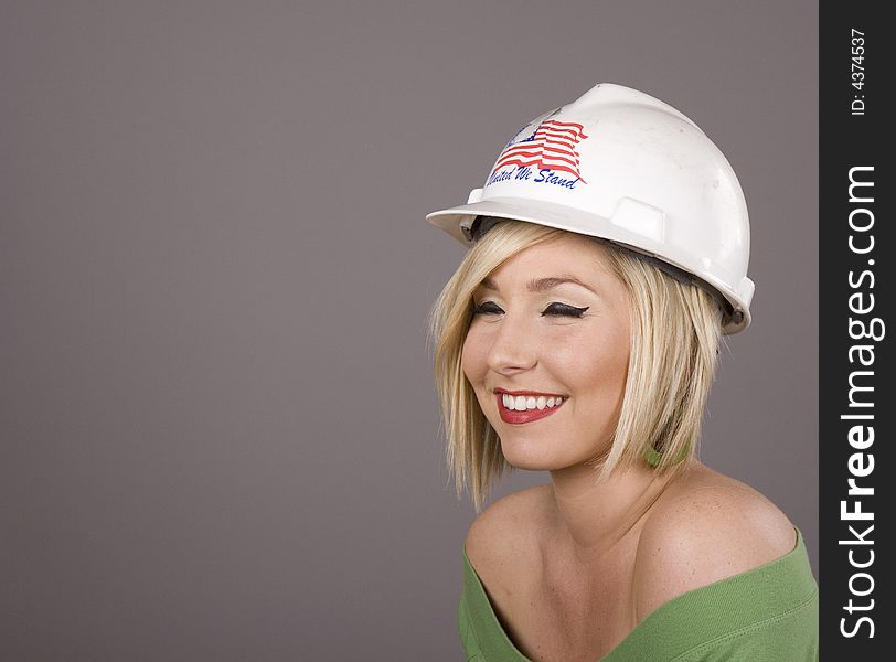 A blonde model in a hard hat on grey background with eyes closed smiling. A blonde model in a hard hat on grey background with eyes closed smiling