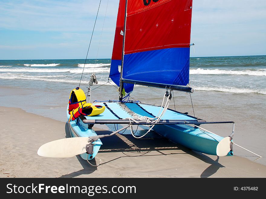 Catamaran on the beach with blue and red sails