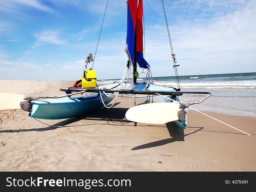 Catamaran on the beach with blue and red sails