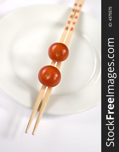 Three cherry tomatoes on a white plate with chopsticks. Three cherry tomatoes on a white plate with chopsticks