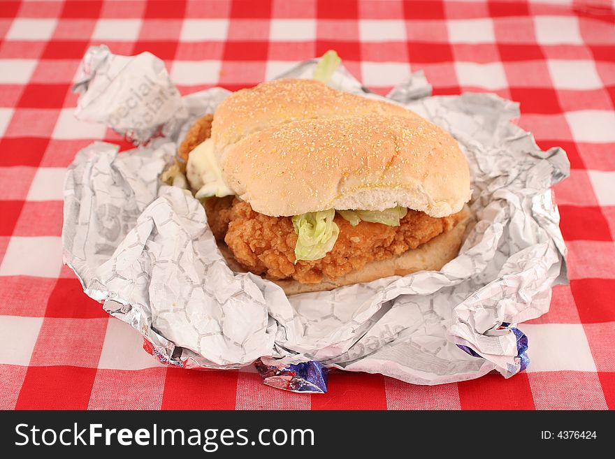 Fast food crispy chicken burger still in wrapper with checkered red background