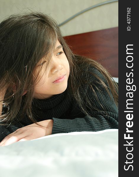 Six year old girl lying on side on bed with sad, serious expression. Six year old girl lying on side on bed with sad, serious expression.