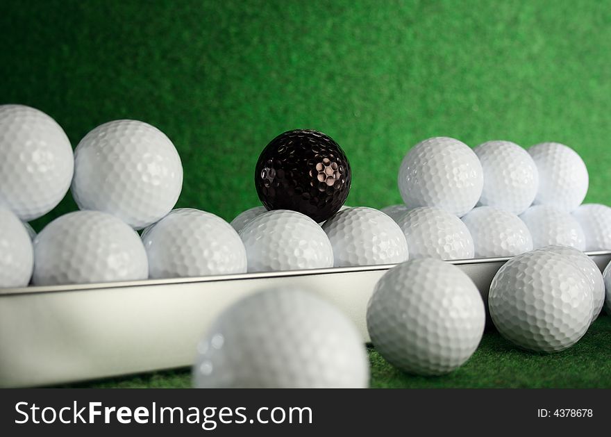 Golfballs with a black joker amongst them.
