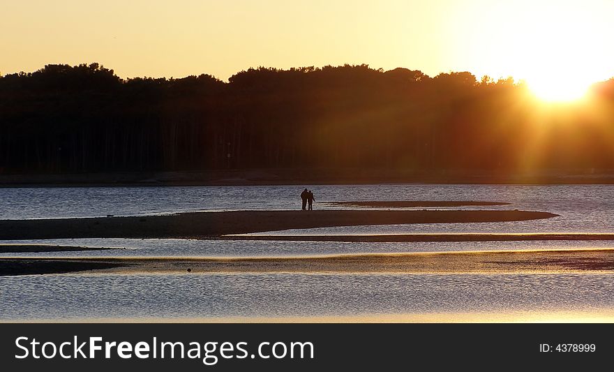 Lovers silhouettes walking by the sea, during low tide at sunset;  suitable for conceptual love and Valentine cards;