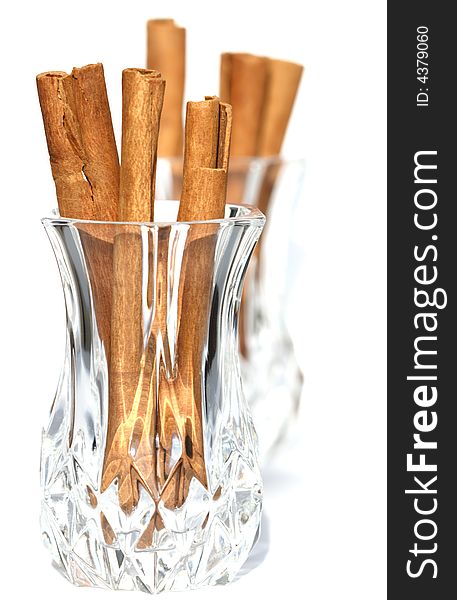 Cinnamon sticks in crystal glass and second one on background, light shadow. Cinnamon sticks in crystal glass and second one on background, light shadow