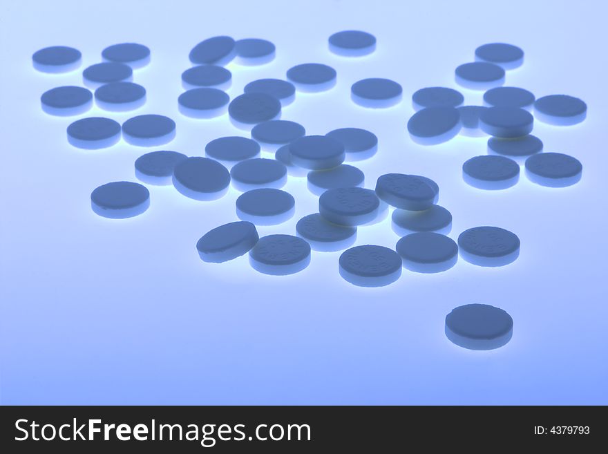 Back-lit close-up of blue toned vitamin pills against a plain background