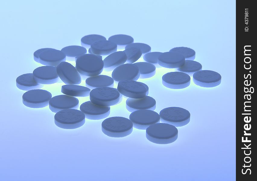 Back-lit close-up of blue toned vitamin pills agains a plain background