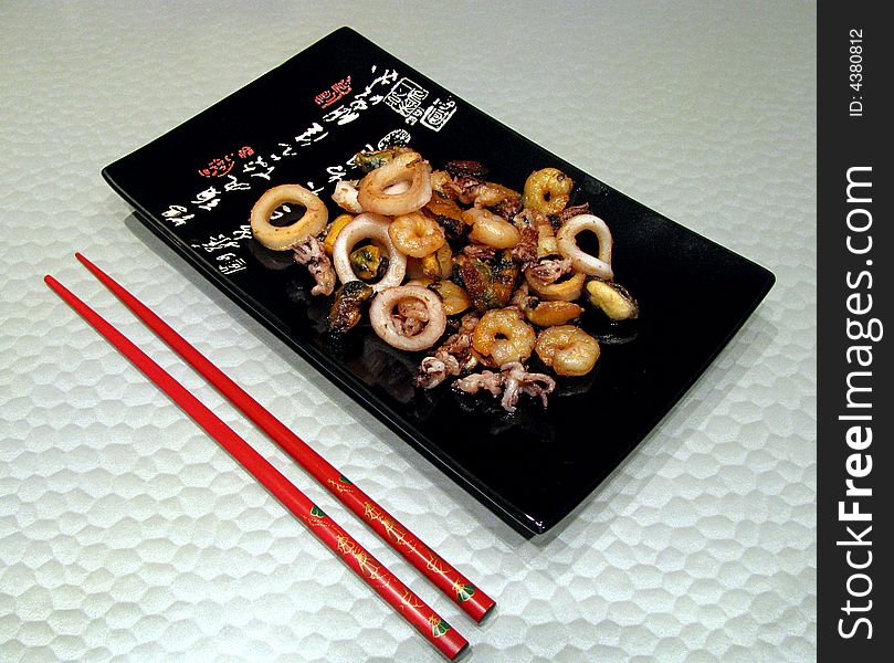 Black square plate with red sticks and sea food. Black square plate with red sticks and sea food