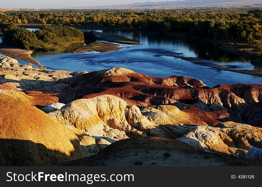 Multicoloured beach located in Xinjiang, China. Under sunset the stone showed as a lot of colors and blue water and trees aside