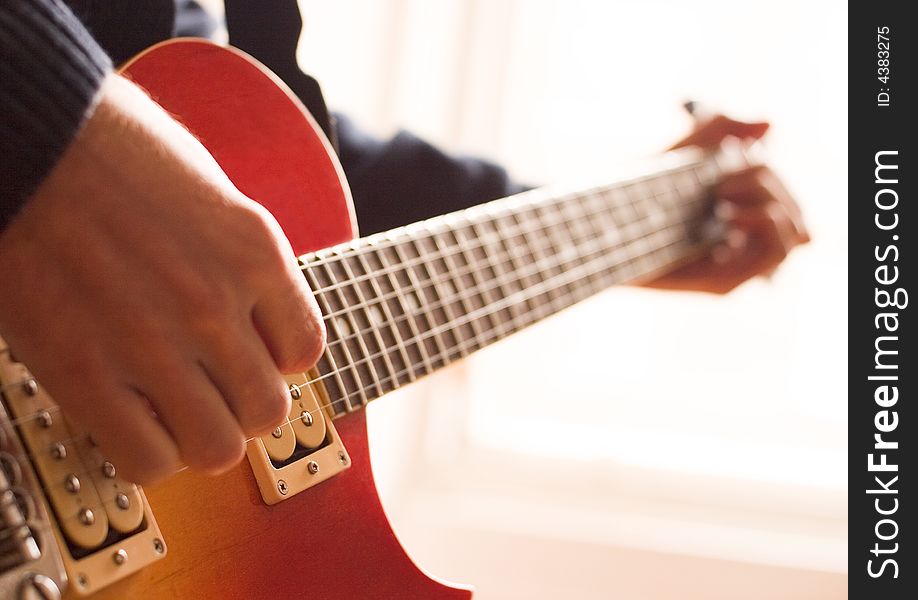 Back-lit closeup of someone practicing the guitar. Shallow depth of field with focus on the guitar body. Back-lit closeup of someone practicing the guitar. Shallow depth of field with focus on the guitar body.