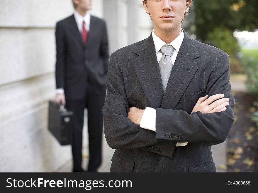 Two businessmen standing in front of building wearing suits looking at camera. Two businessmen standing in front of building wearing suits looking at camera