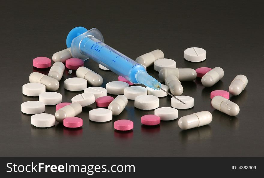 Blue syringe with tablets and pills isolated on a black background. Blue syringe with tablets and pills isolated on a black background