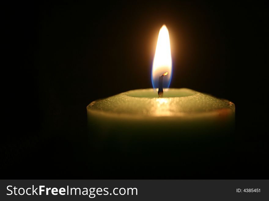 A  close up of a green candle burning in the dark. A  close up of a green candle burning in the dark