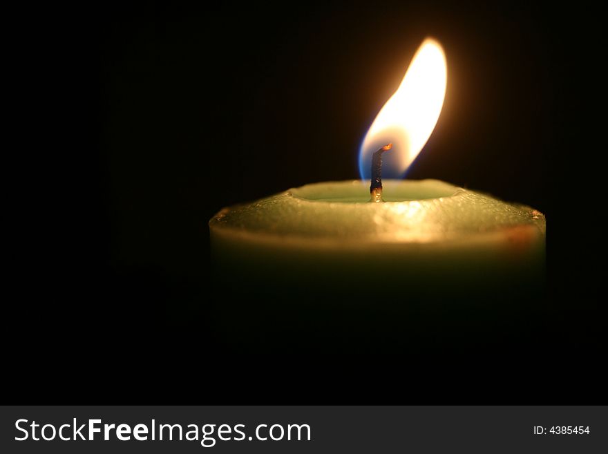 A  close up of a green candle burning in the dark. A  close up of a green candle burning in the dark