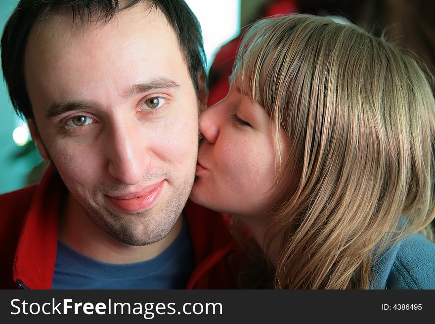 Young woman kisses smiling man. Young woman kisses smiling man