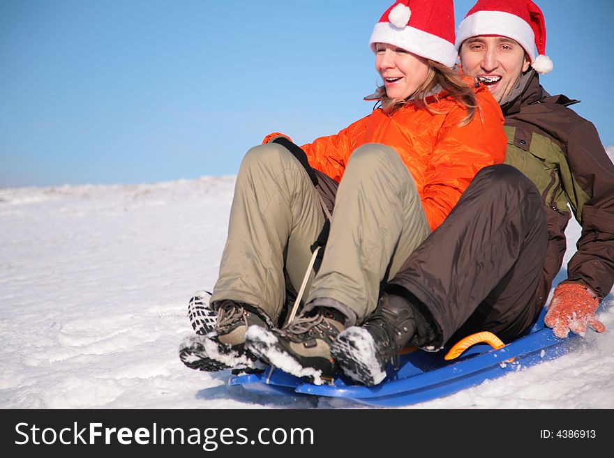 Man and woman in santa claus hats ride on sled
