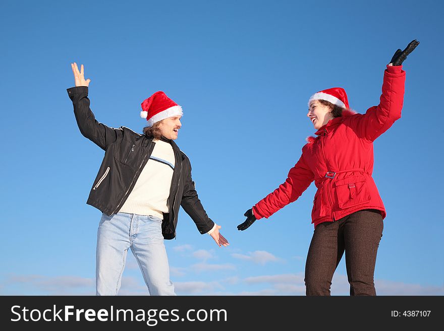 Couple dance in santa claus hats against blue sky