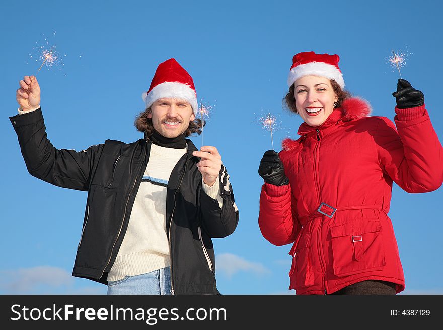 Couple against blue sky background in winter in santa claus hats with sparklers. Couple against blue sky background in winter in santa claus hats with sparklers