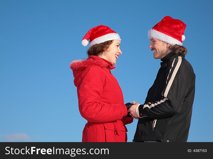 Couple against blue sky background in winter in santa claus hats stand face to face