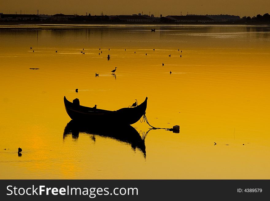 Sunset at the River Tagus Estuary, Portugal, EU. Traditional fishing boat is anchored and wild life birds in the shallows. Sunset at the River Tagus Estuary, Portugal, EU. Traditional fishing boat is anchored and wild life birds in the shallows.