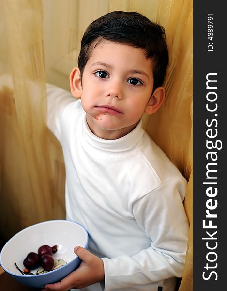 A view with a little boy eating cherries from a bowl