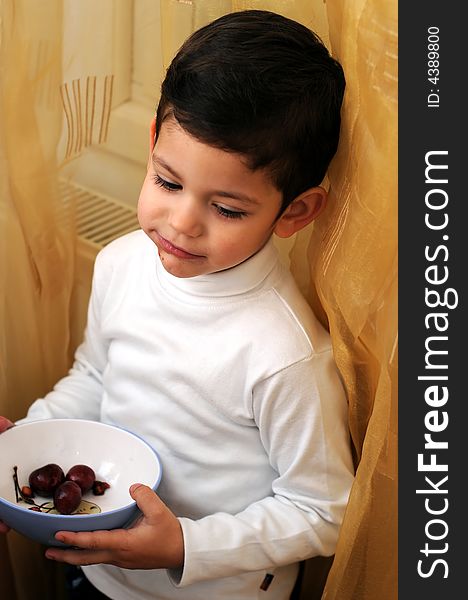 A view with a little boy eating cherries from a bowl