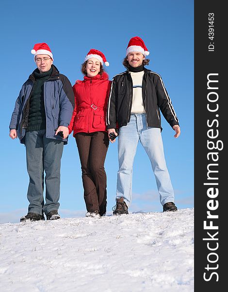 Three friends stand on snow in santa claus hats