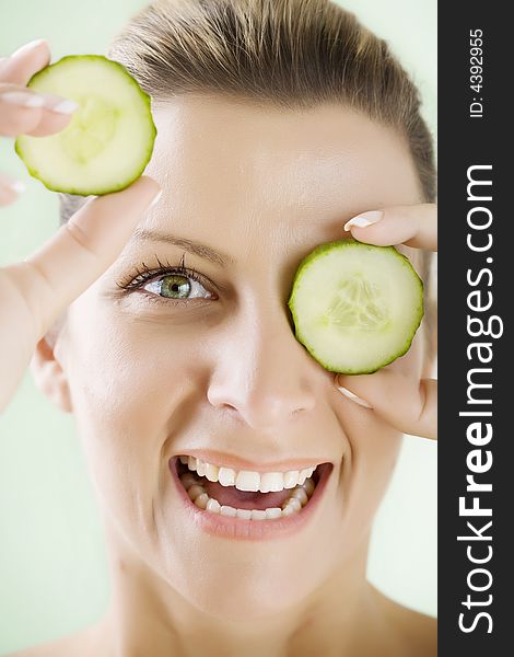 Smiling woman holding cucumber-slices in front of her eye. Smiling woman holding cucumber-slices in front of her eye