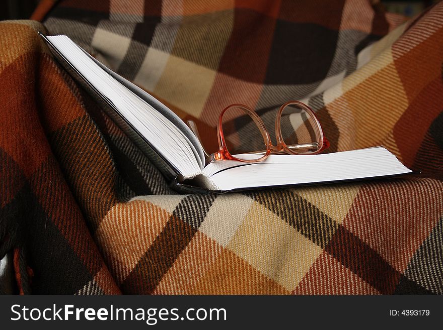 Open book and spectacles lying on chequered plaid. Open book and spectacles lying on chequered plaid