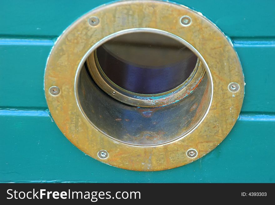 Brass porthole in the hull of a timber yacht.