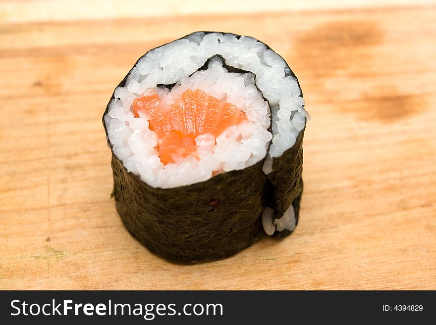 Closeup of sushi roll with salmon on cutting board.
