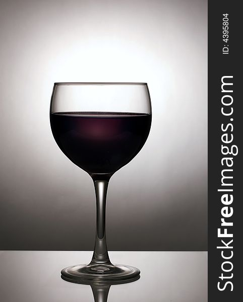 Image of a glass of dark wine silhouetted against spotlight on background. Image of a glass of dark wine silhouetted against spotlight on background