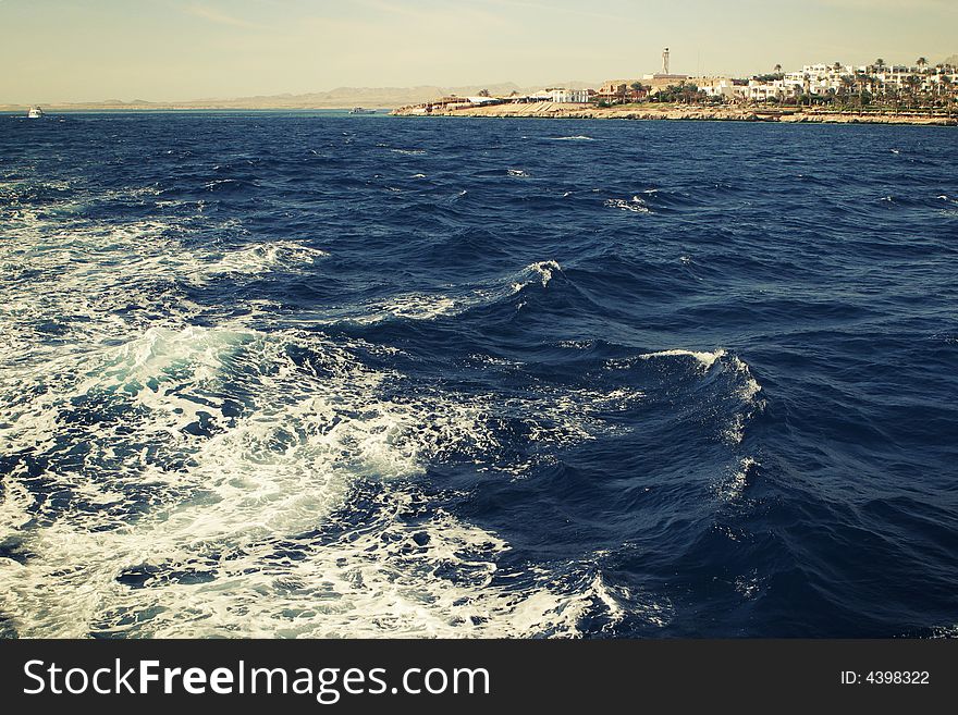 Dark blue sea with foam and short view to the coast