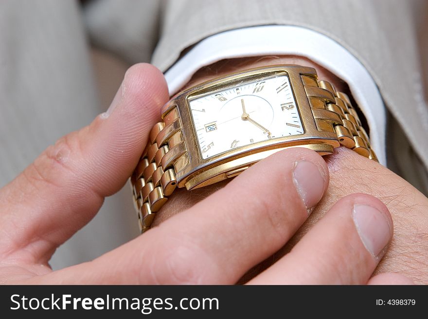A golden watch on the hand of a man in a light suit. A golden watch on the hand of a man in a light suit