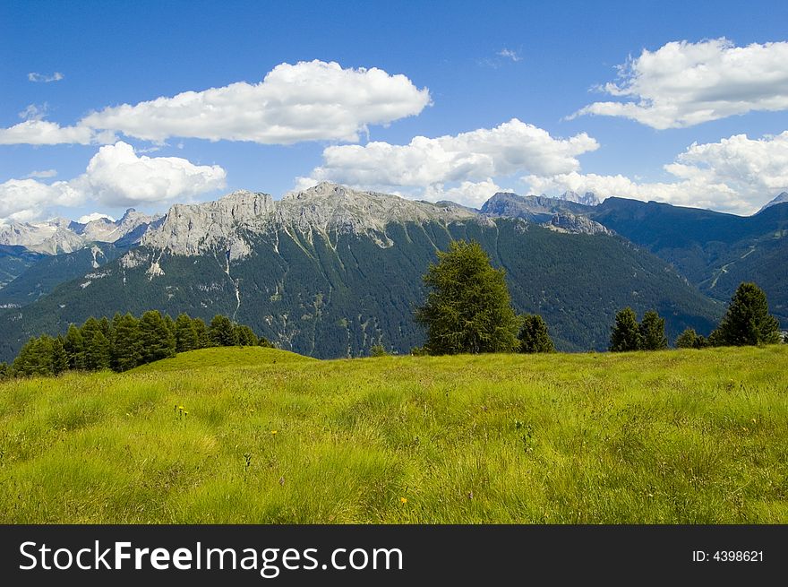 View of dolomites mountains with green gras, blue sky and white clouds