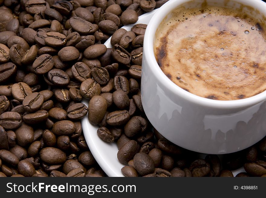 Cup of espresso with froth surrounded by coffee beans