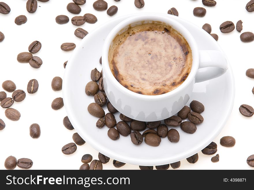 Cup of espresso with froth surrounded by coffee beans