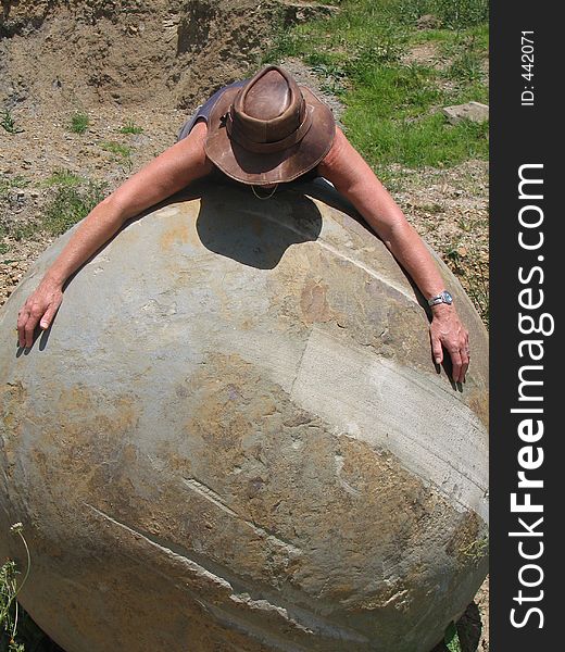 Person draped around a limestone /basalt rock ball uncovered on farmland in a quarry.perhaps from early volcanic eruption. Person draped around a limestone /basalt rock ball uncovered on farmland in a quarry.perhaps from early volcanic eruption
